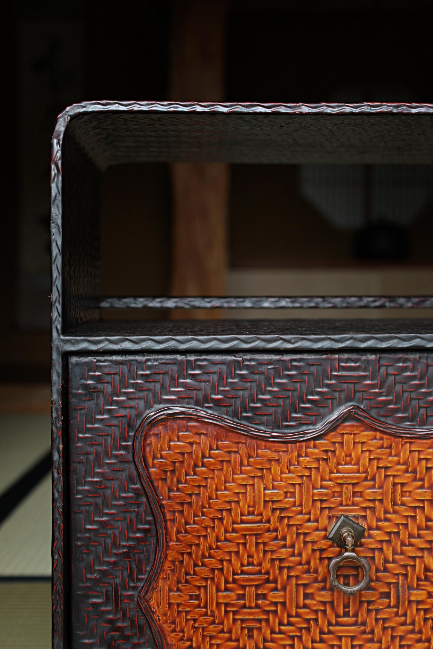 a close-up view of a wooden cabinet with a woven texture, featuring a metal handle and a curved design.