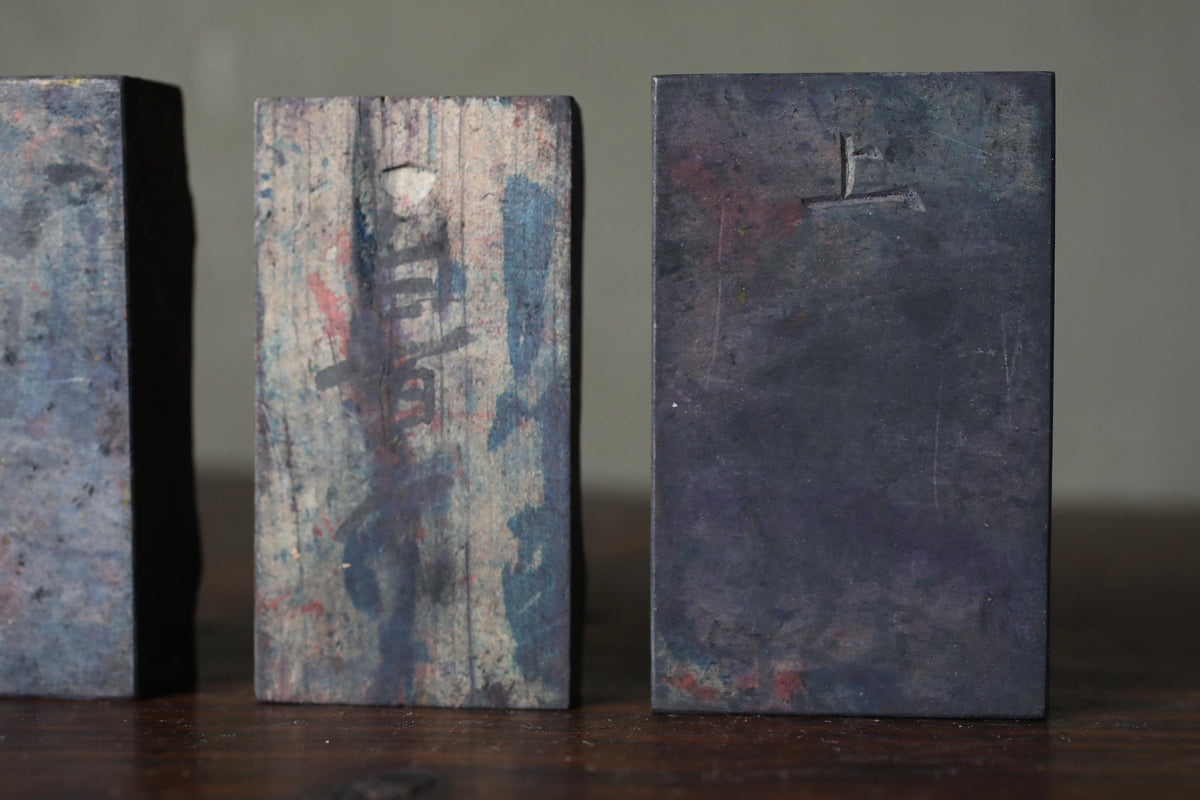 three rectangular objects with varying textures and colors, including a dark, weathered piece of wood and two metal blocks.