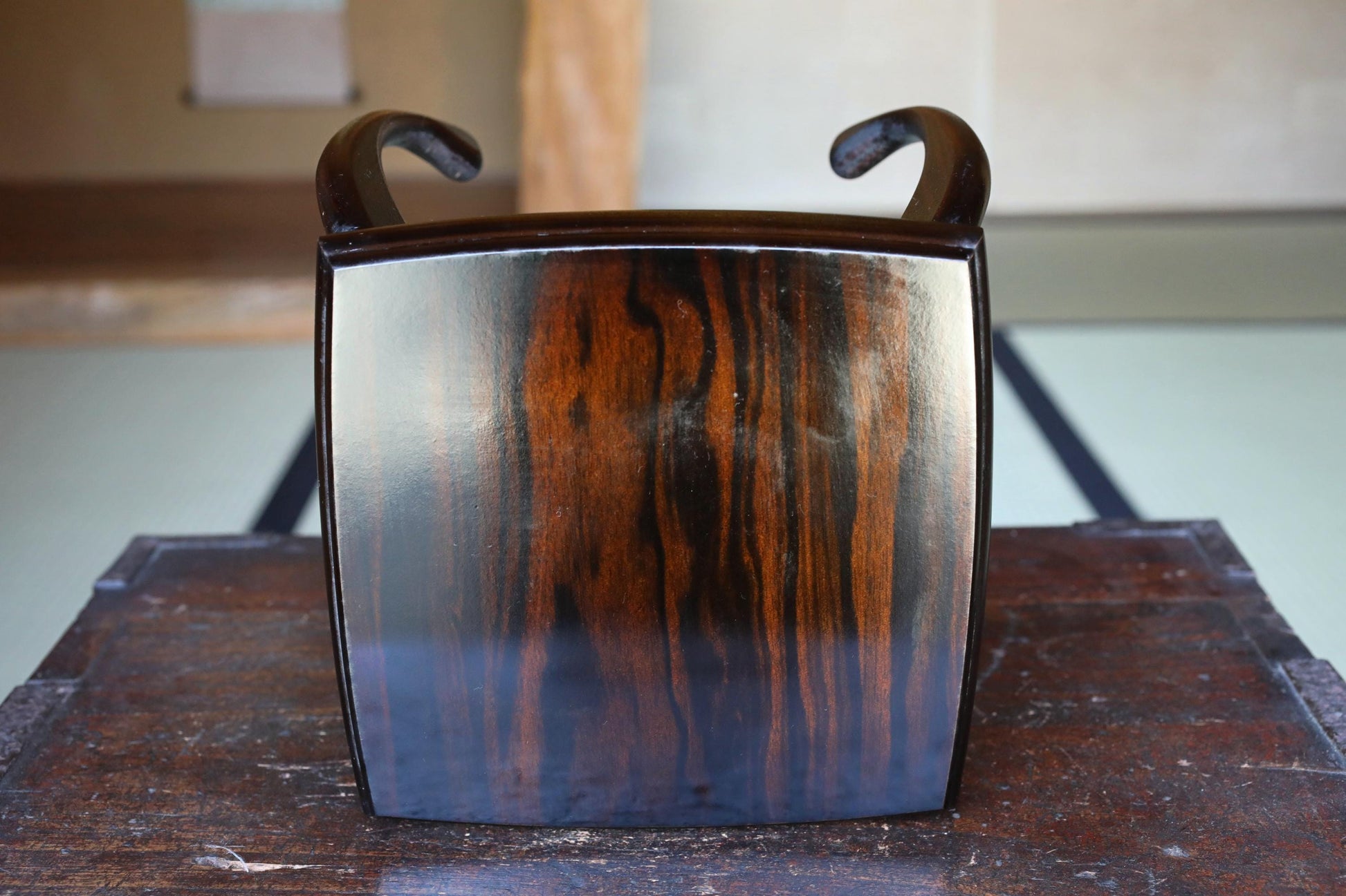 a wooden object with a dark finish, featuring a textured pattern and two curved handles on either side.