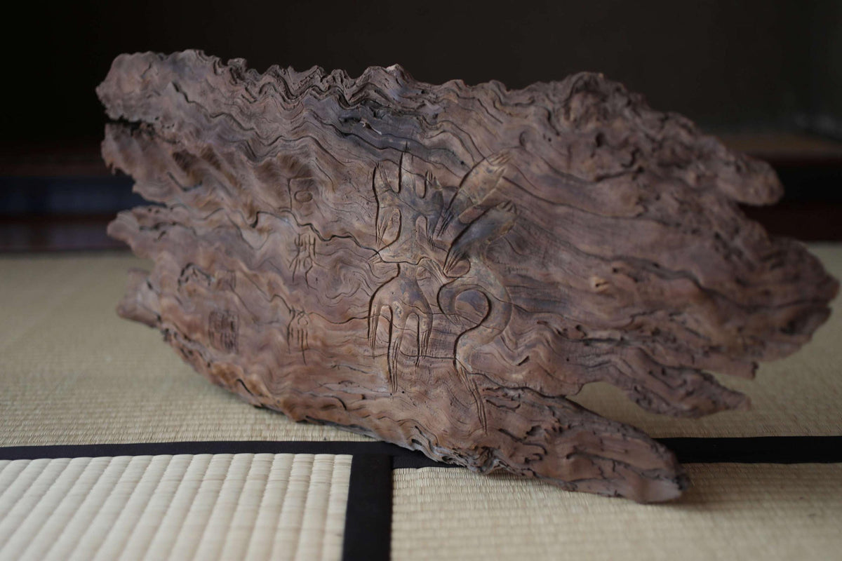 a wooden sculpture with intricate carvings on its surface, resting on a mat.