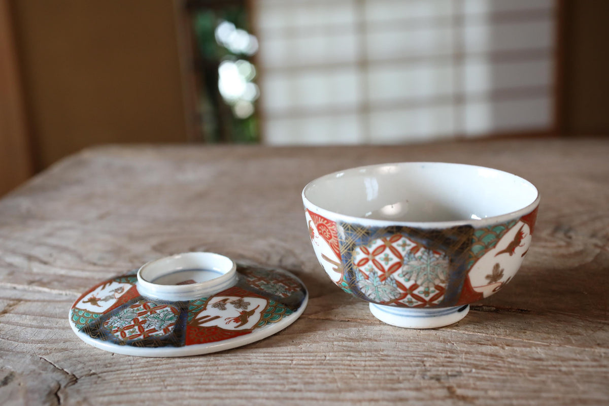 a wooden table with a white bowl and a matching lid, both adorned with intricate red and blue designs.