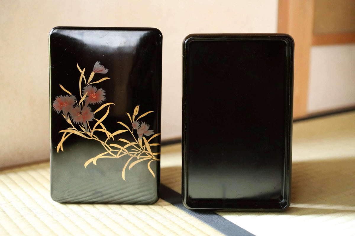 two black rectangular boxes with floral designs on them, placed side by side on a surface.