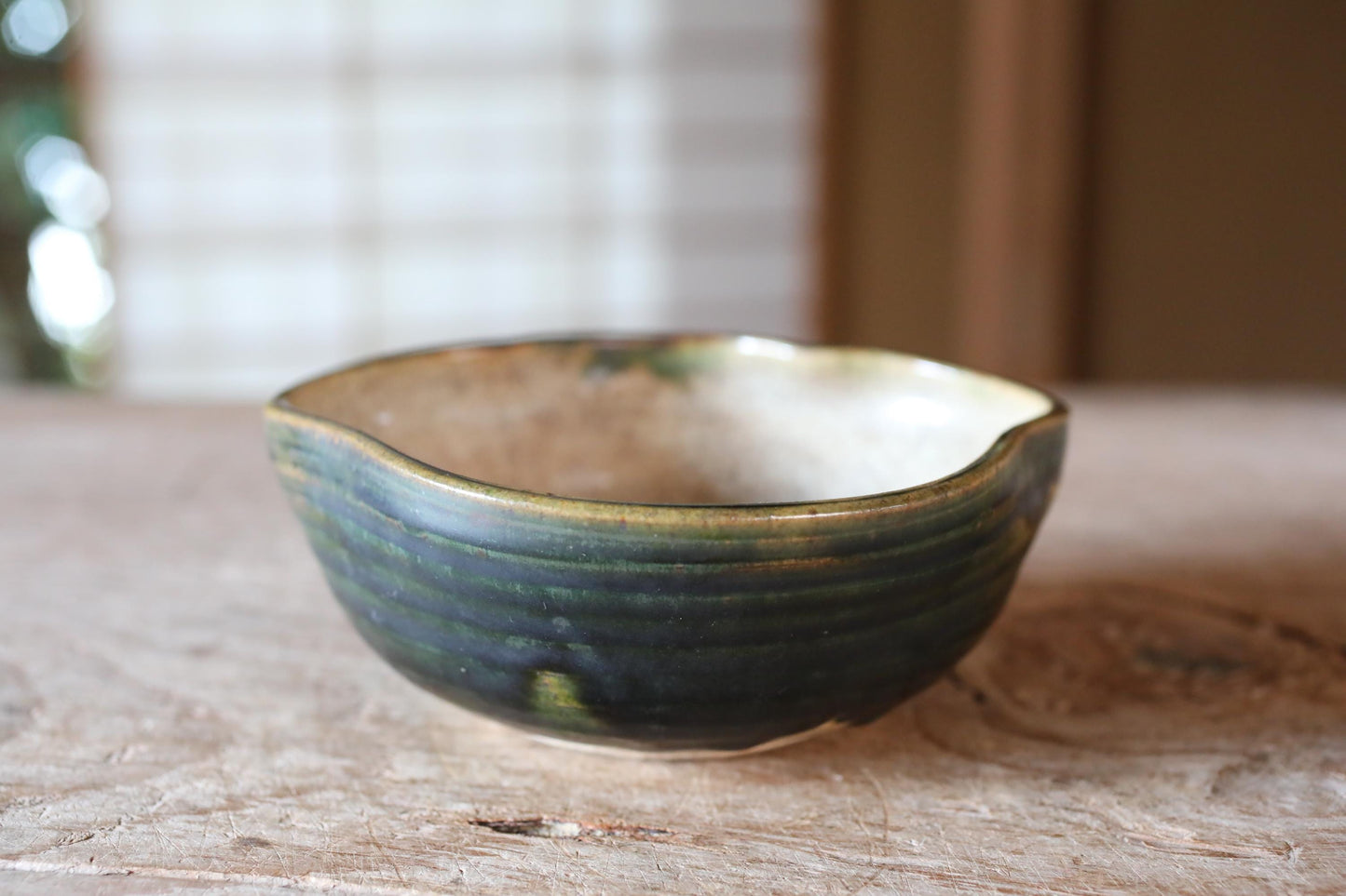 A ceramic bowl with a green and white glaze sits on a wooden surface.