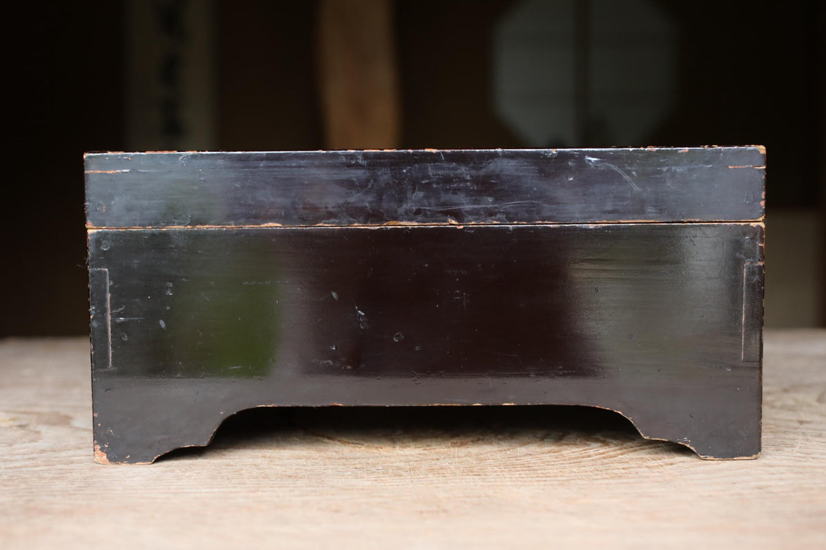 A dark wooden box with a glossy finish sits on a wooden surface.