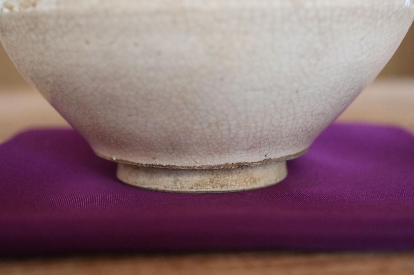 A close-up view of a white ceramic bowl with a textured surface, resting on a purple cloth or fabric.