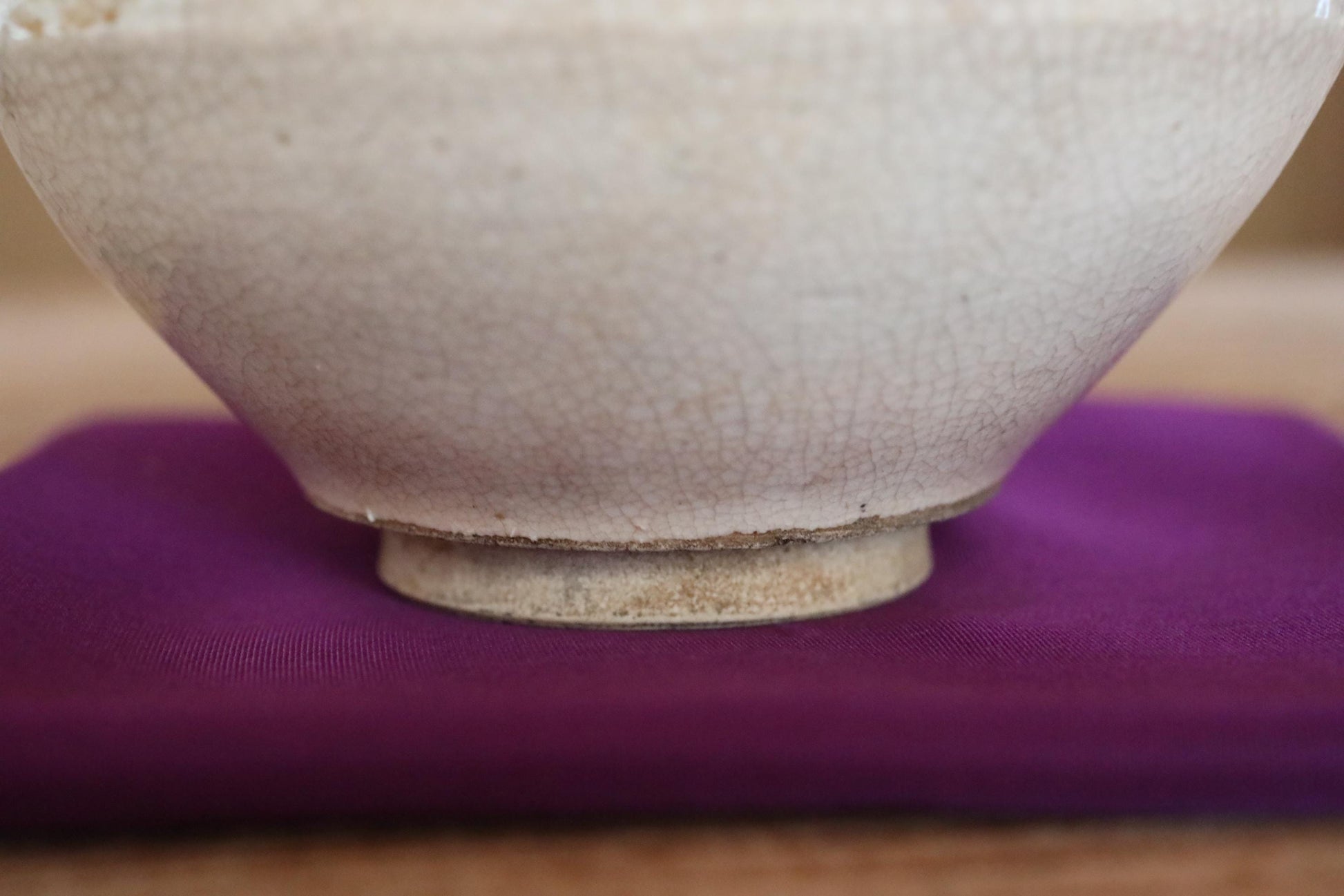 A close-up view of a white ceramic bowl with a textured surface, resting on a purple cloth or fabric.