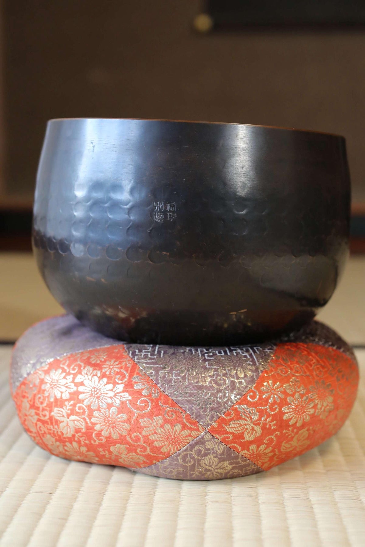a black bowl placed on top of a colorful cushion or pillow with an intricate floral pattern.