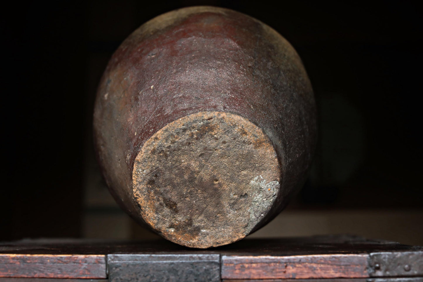 An old, rusted clay pot sits on a wooden surface, its weathered surface and dark color suggesting it has been exposed to the elements for a long time.
