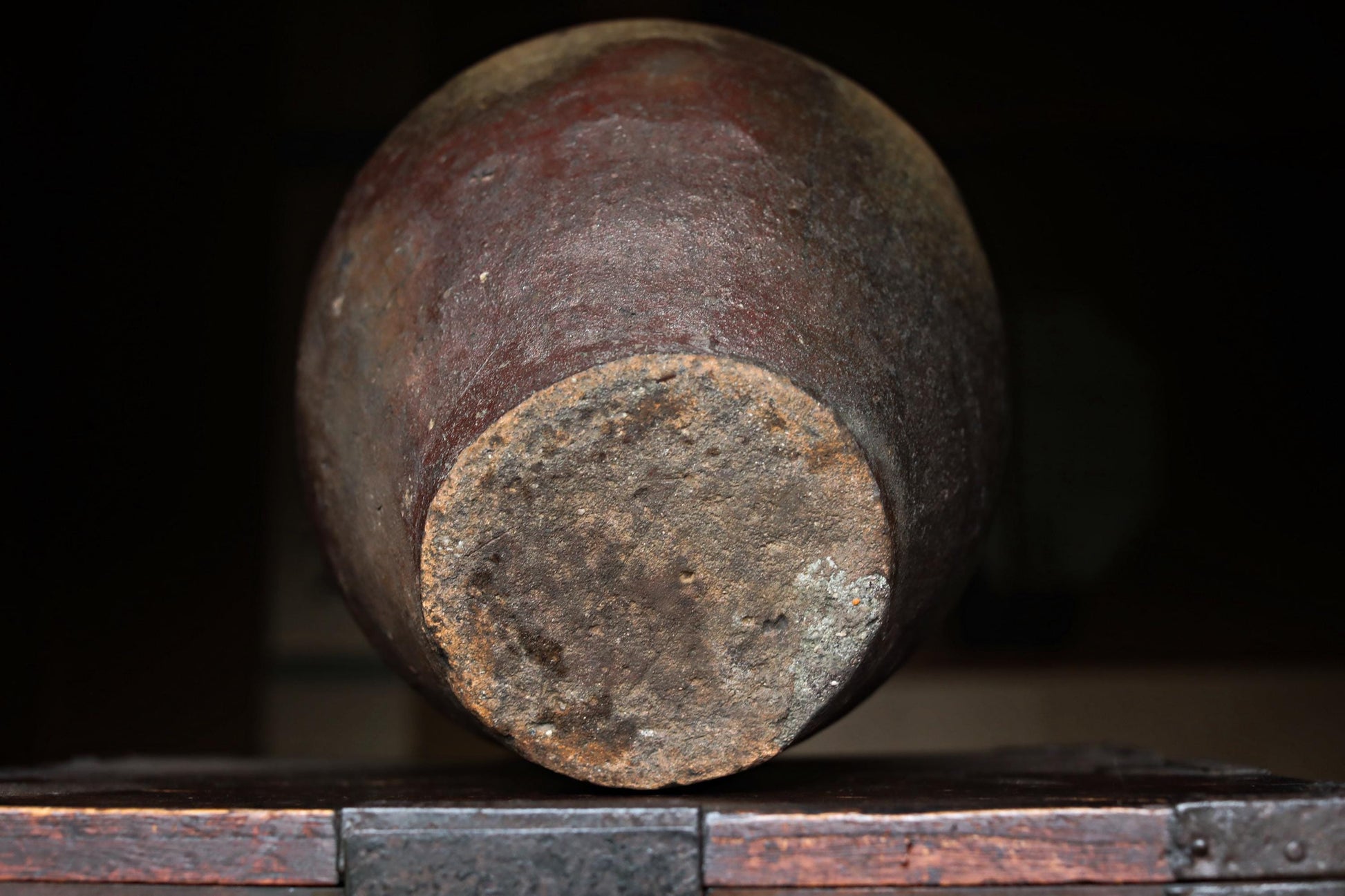 An old, rusted clay pot sits on a wooden surface, its weathered surface and dark color suggesting it has been exposed to the elements for a long time.