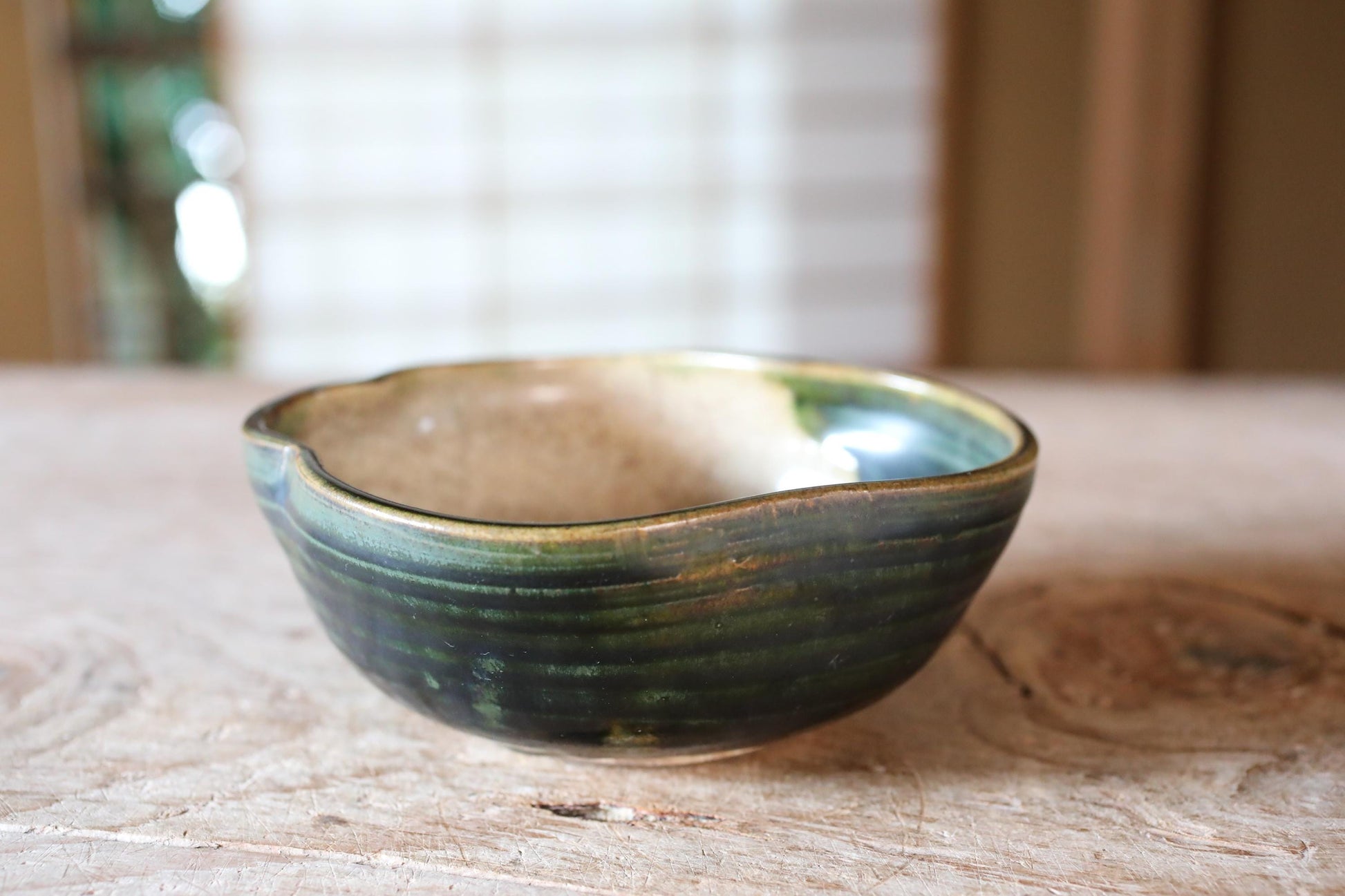 A ceramic bowl with a green and brown glaze sits on a wooden surface.