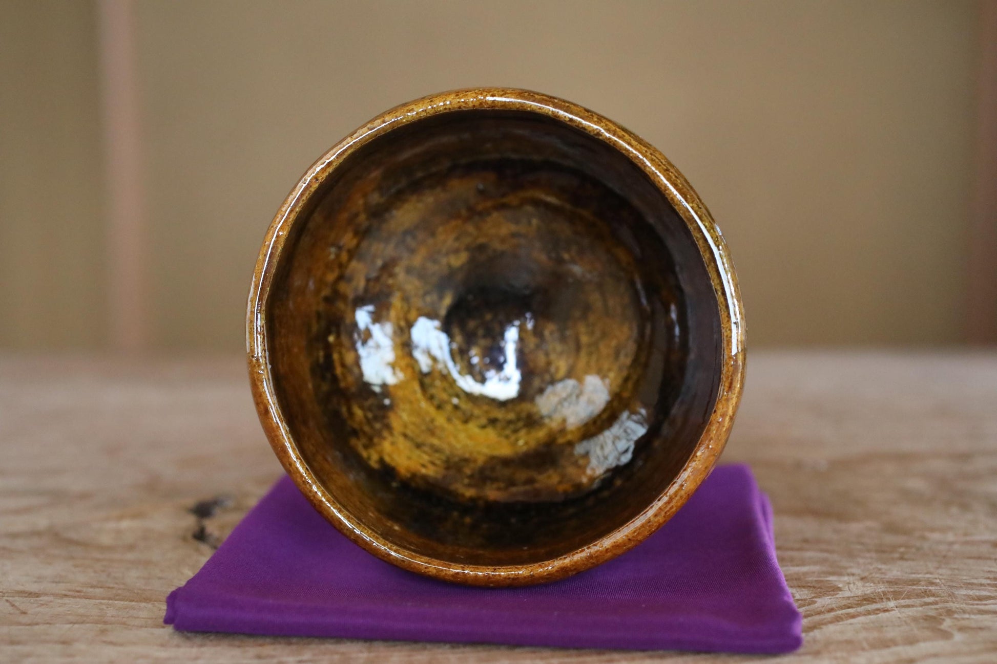 A brown ceramic bowl with a curved rim sits on a purple cloth on a wooden surface.