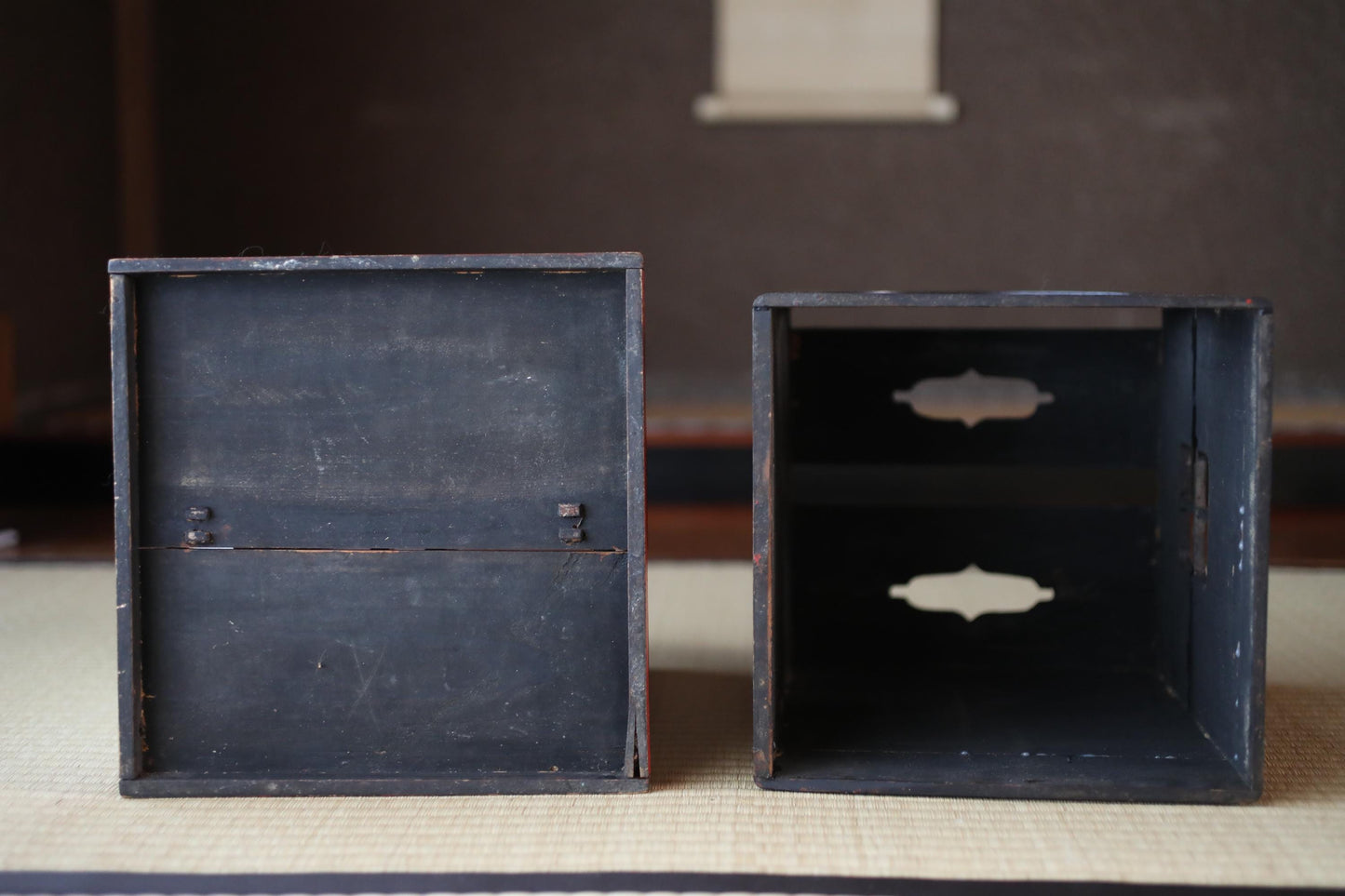 Two black wooden boxes with visible signs of wear and tear, placed side by side on a woven mat.