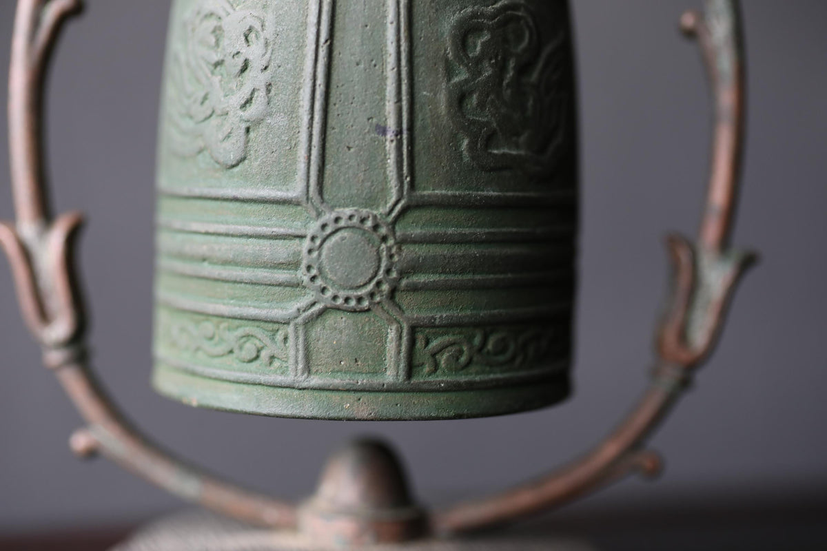 A close-up view of a green metal bell with intricate designs on its surface, mounted on a metal stand.