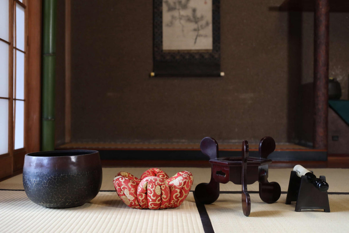 a traditional Japanese room with a wooden floor, a black bowl, a red and white bowl, and a wooden stool.