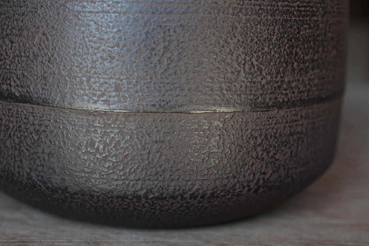A close-up view of a textured, dark-colored metal surface, possibly a piece of pottery or a decorative item.