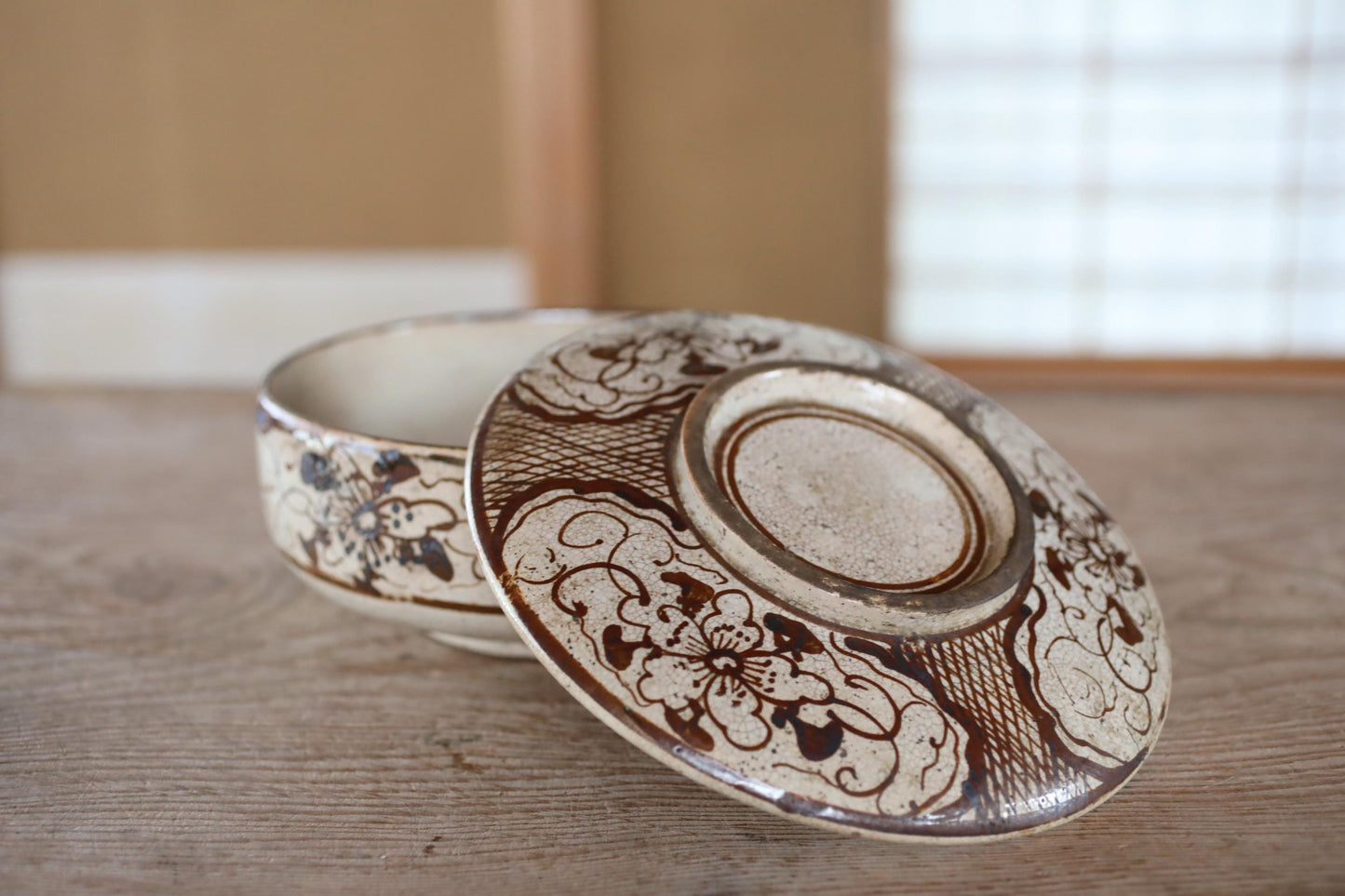 a close-up of a decorative ceramic bowl and its lid, both adorned with intricate floral patterns, resting on a wooden surface.