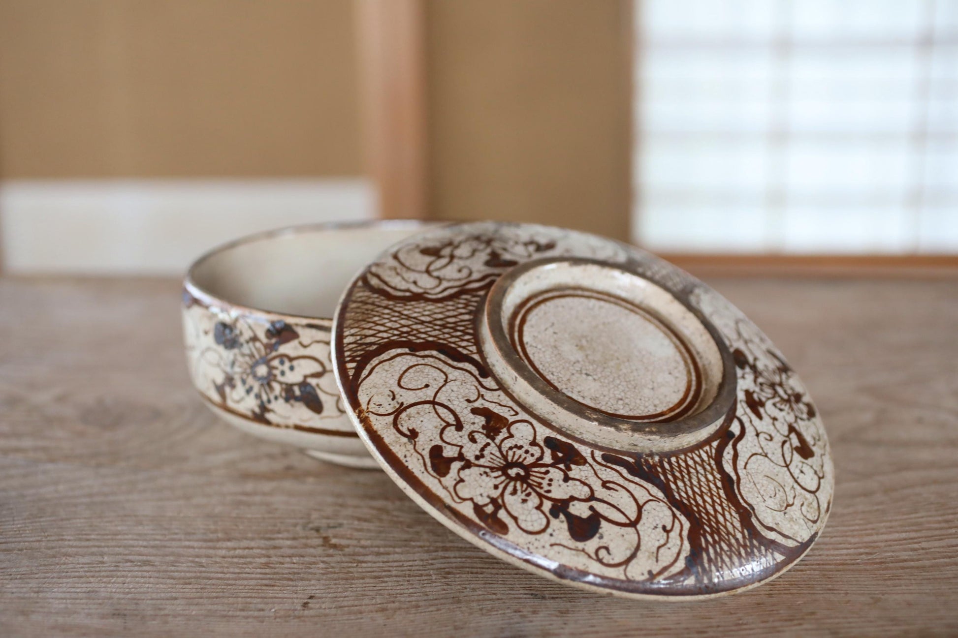 a close-up of a decorative ceramic bowl and its lid, both adorned with intricate floral patterns, resting on a wooden surface.