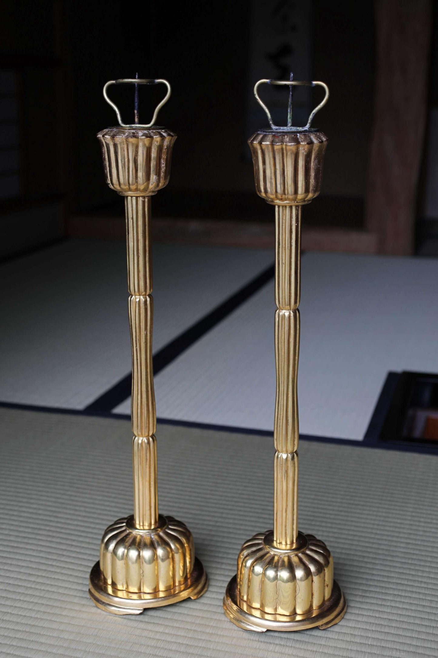Two ornate gold candlesticks with handles on top, standing upright on a white surface.