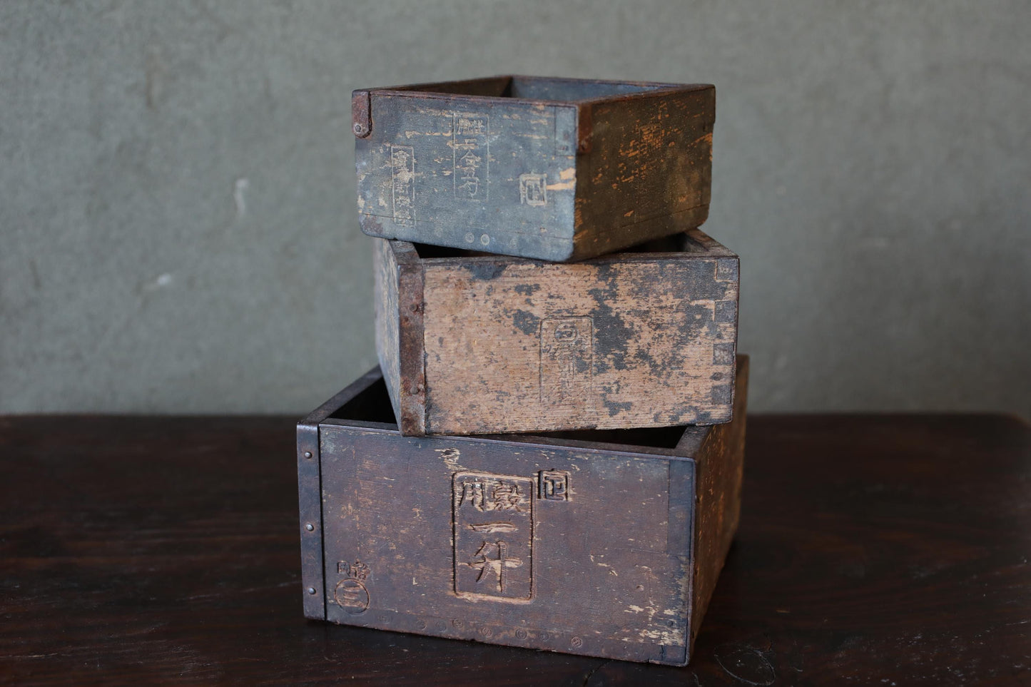 A stack of three old, weathered wooden boxes on a dark surface.