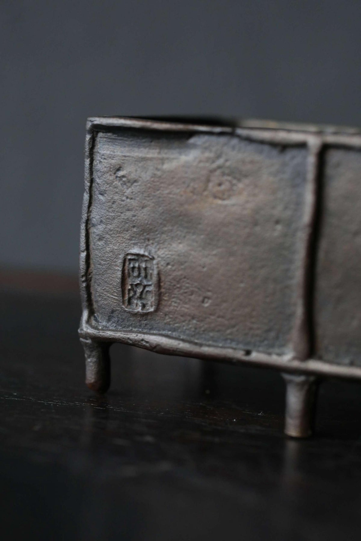 A close-up image of a metal object, possibly a sculpture or a container, with a textured surface and a small emblem or symbol on it.