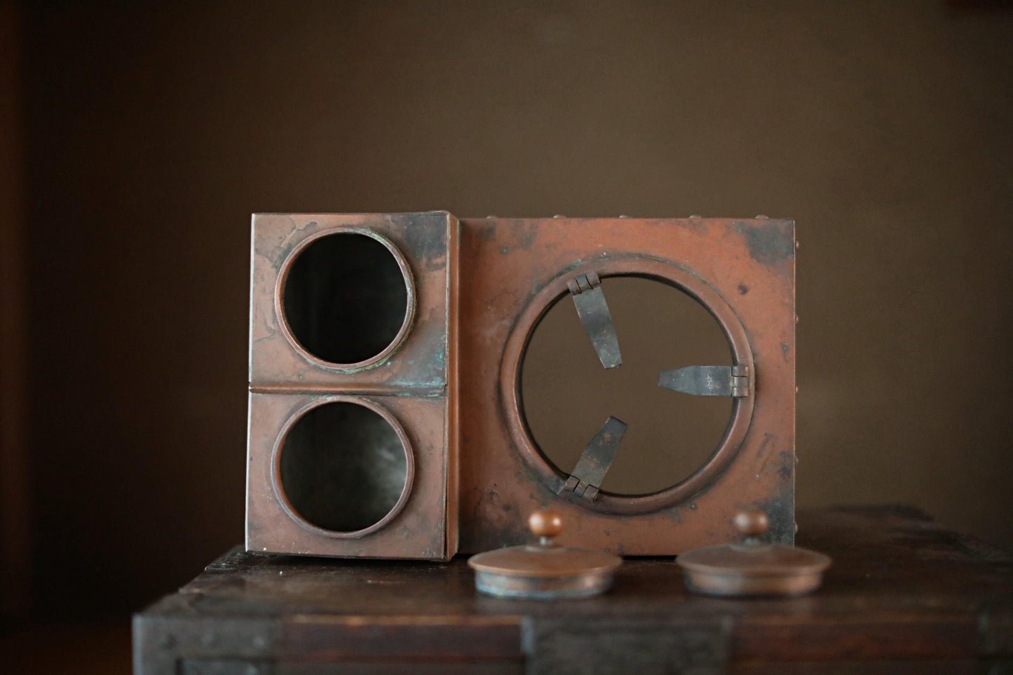 an old, rusted metal object with a circular opening and two circular holes, sitting on a wooden surface.