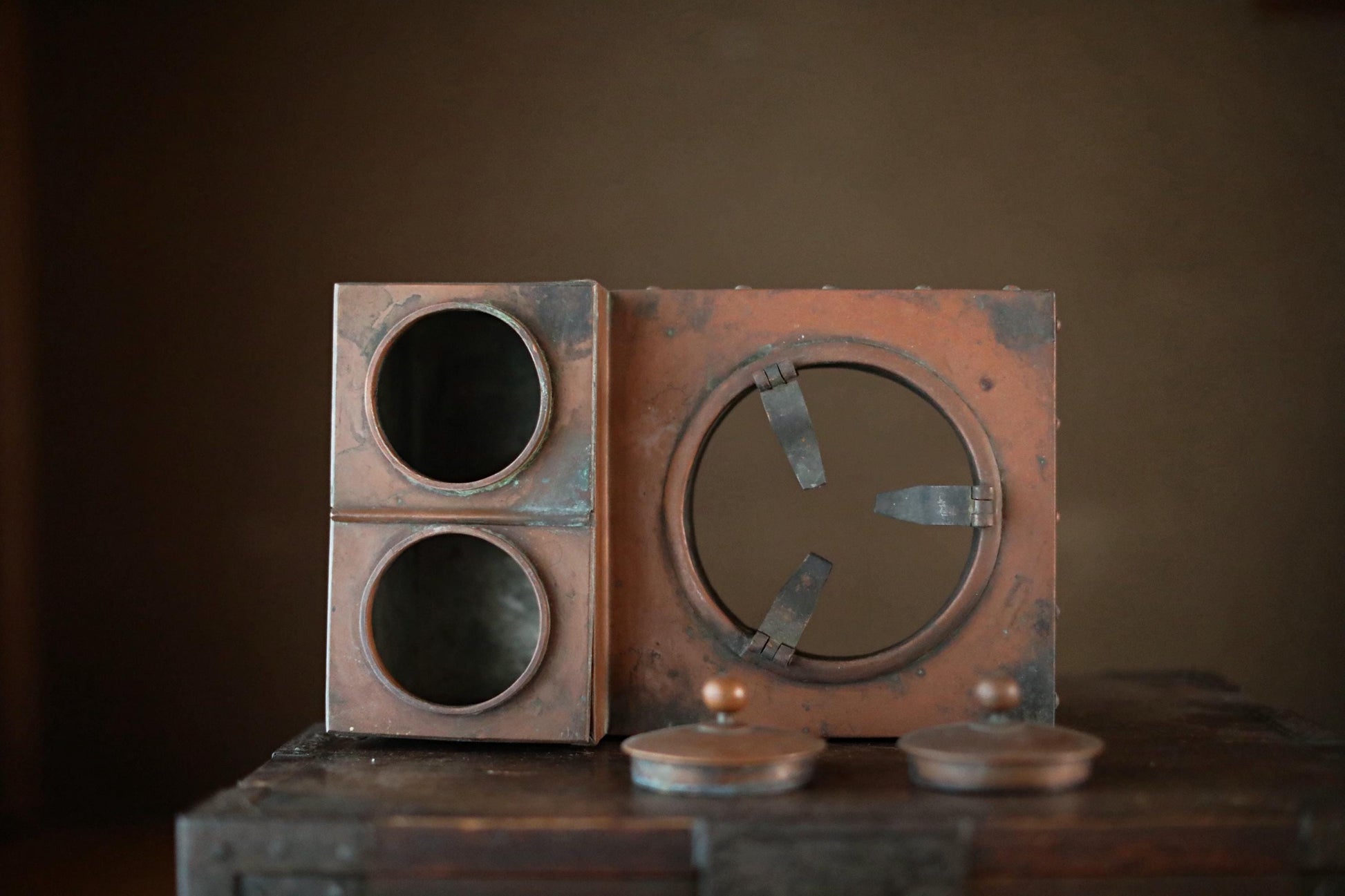 an old, rusted metal object with a circular opening and two circular holes, sitting on a wooden surface.