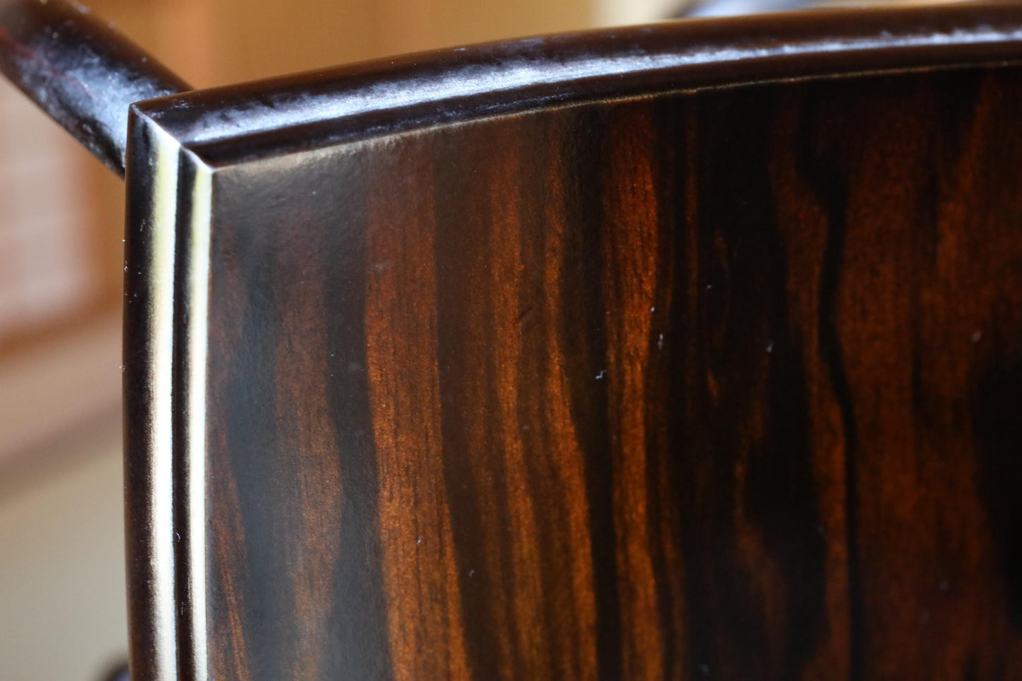a close-up view of a dark wooden surface, possibly a chair or table, with a rich, dark brown color and a textured, wood-like appearance.