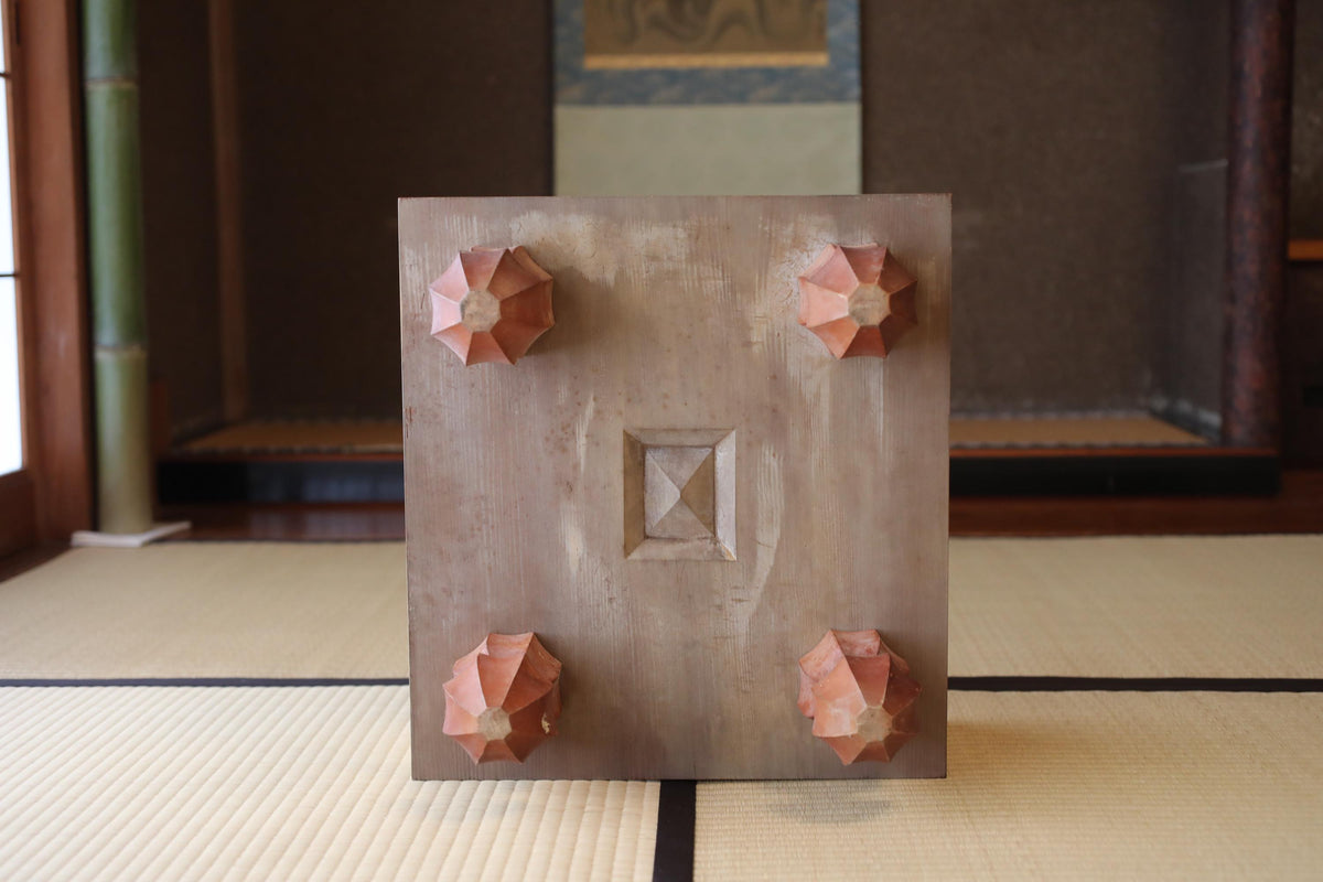 a wooden object with four triangular or octagonal shapes on its surface, placed on a tatami mat.