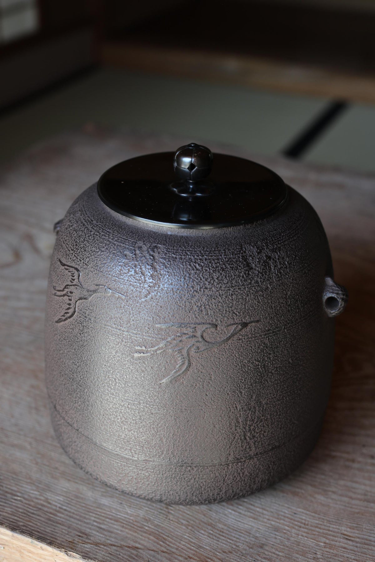 A ceramic teapot with a black lid sits on a wooden surface.