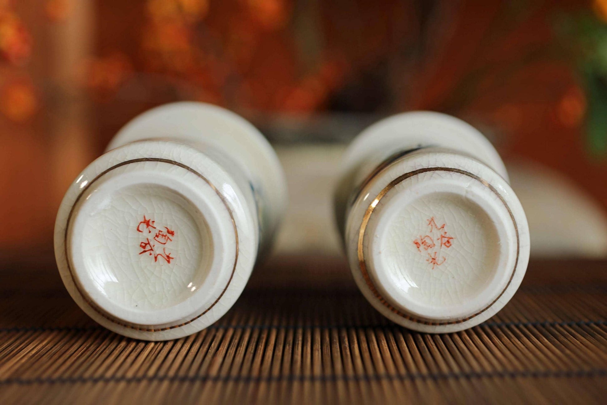 Two white ceramic cups with red designs on their bases are placed on a wooden surface.