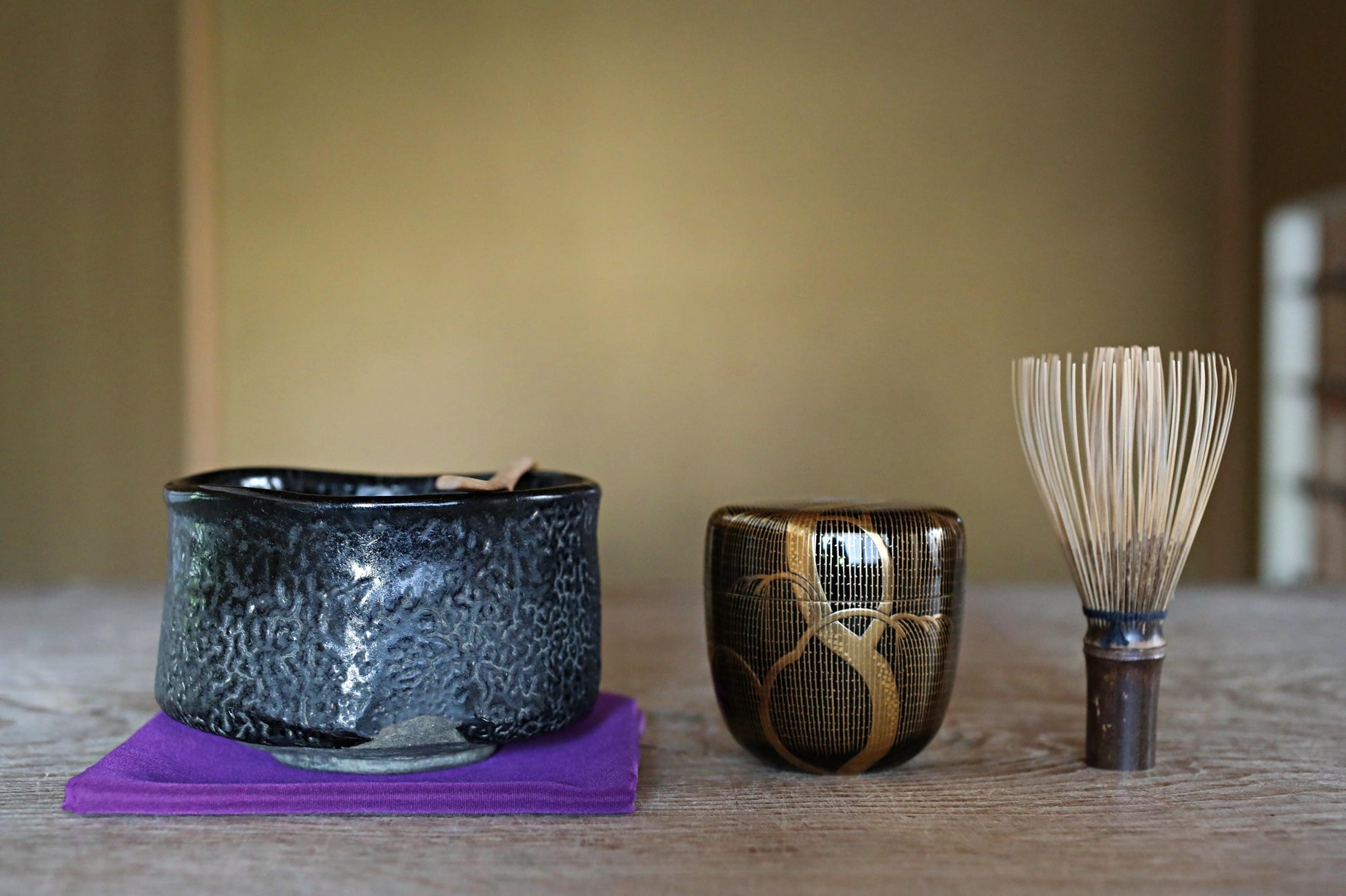 a black ceramic bowl, a black and gold ceramic cup, and a white and brown brush on a wooden surface.