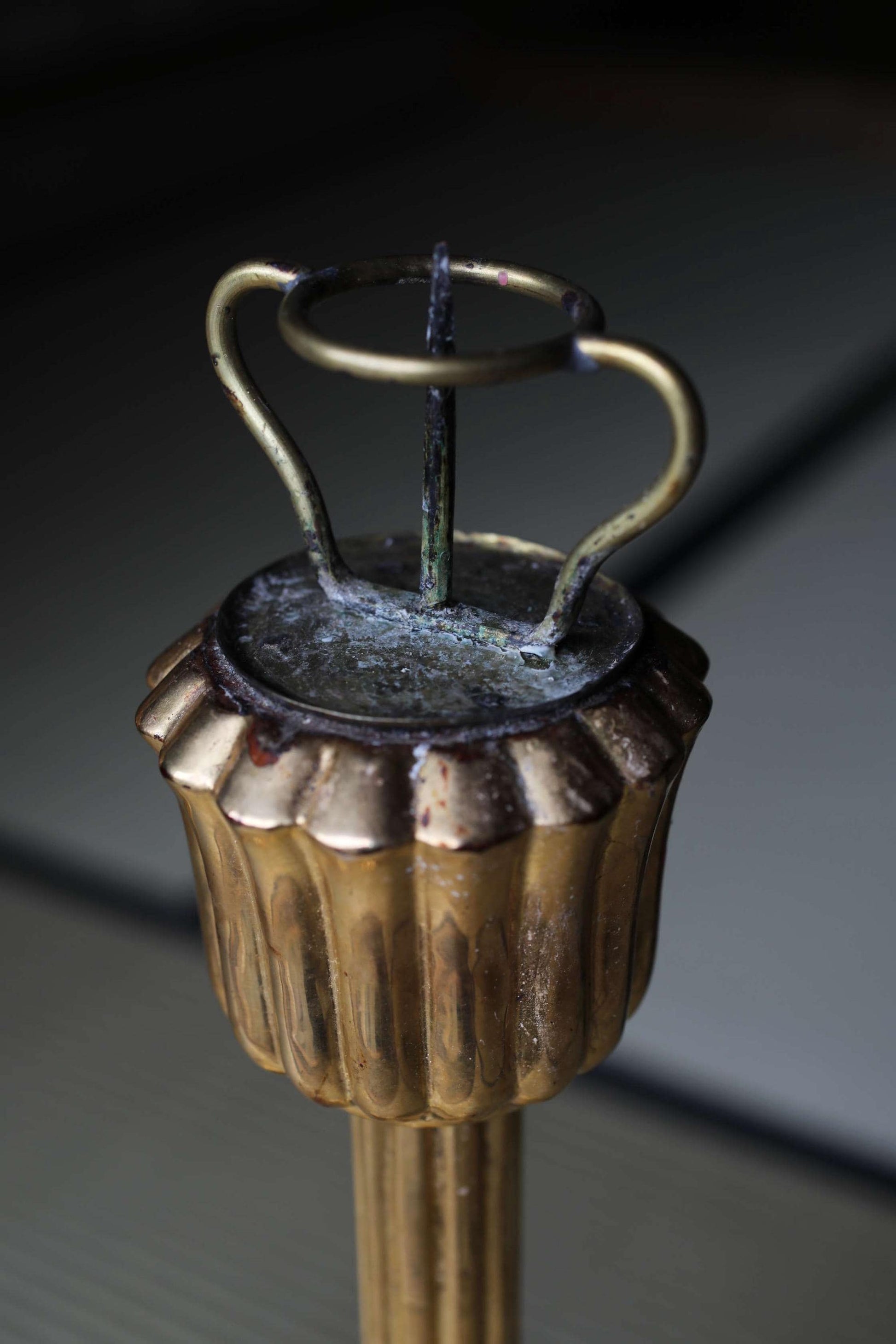 A close-up view of a gold-colored metal candlestick holder with a circular top and a curved handle.