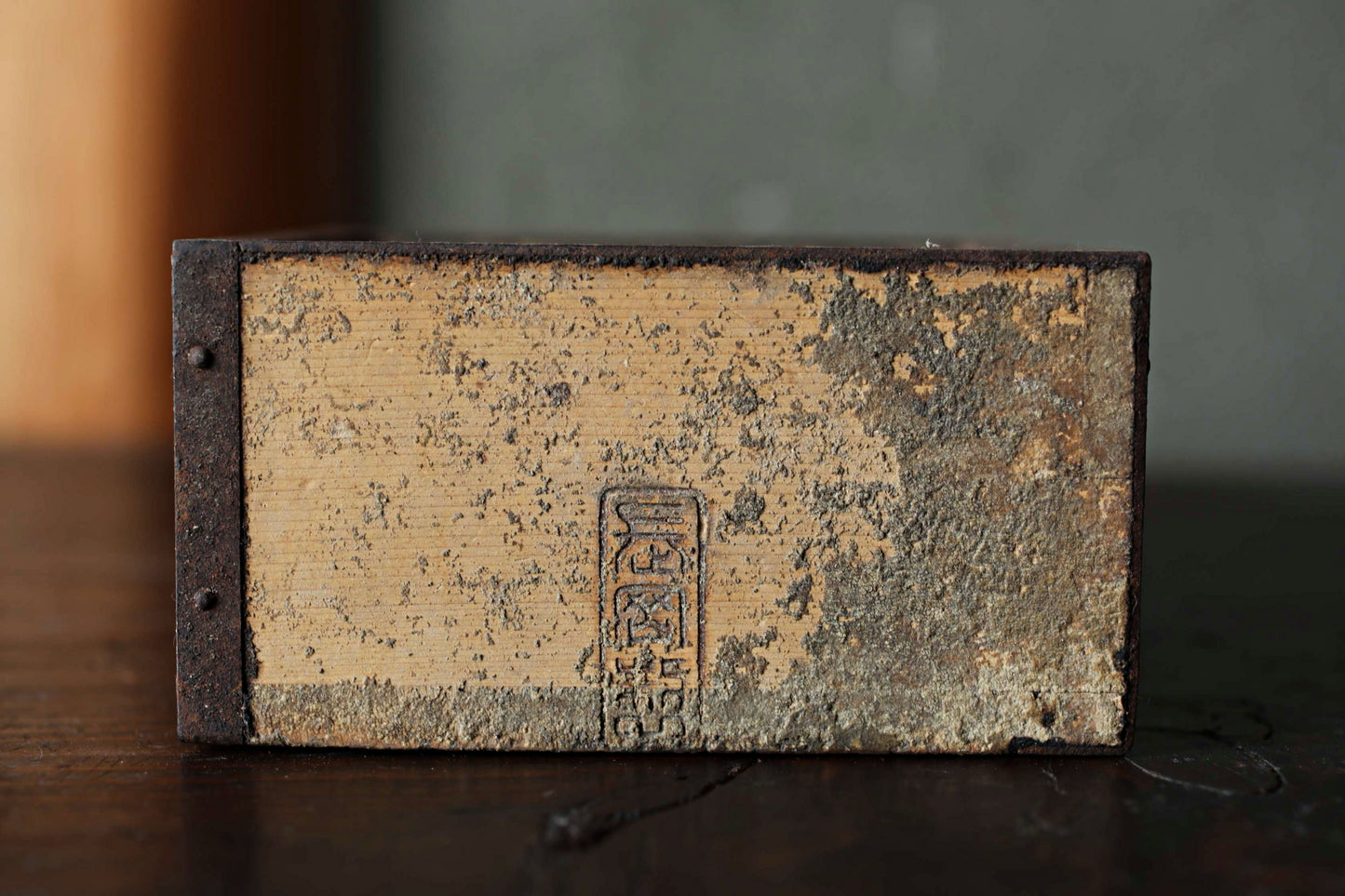 a weathered, wooden object with a metal frame, sitting on a dark surface.