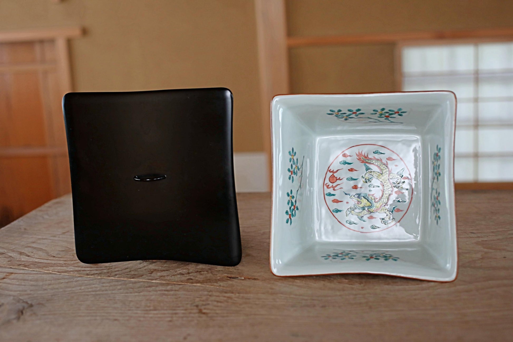 a black square object and a white square object with a colorful floral design on them, both placed on a wooden surface.