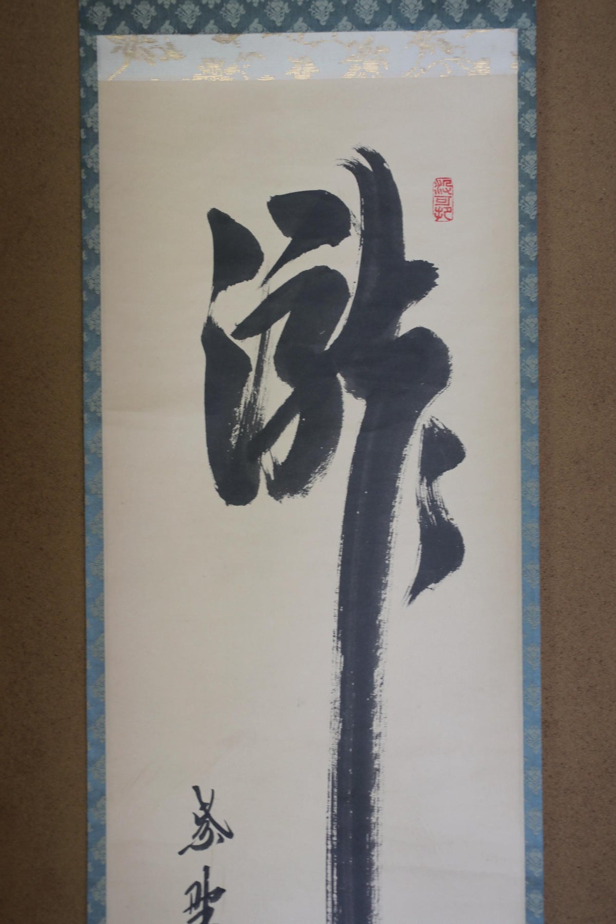 a large, abstract black and white painting with a prominent brush stroke in the center. The painting appears to be a traditional Chinese scroll or banner, with a floral border around the edges. The artwork is displayed on a wall, and there is a small amount of text visible in the bottom left corner of the image.
