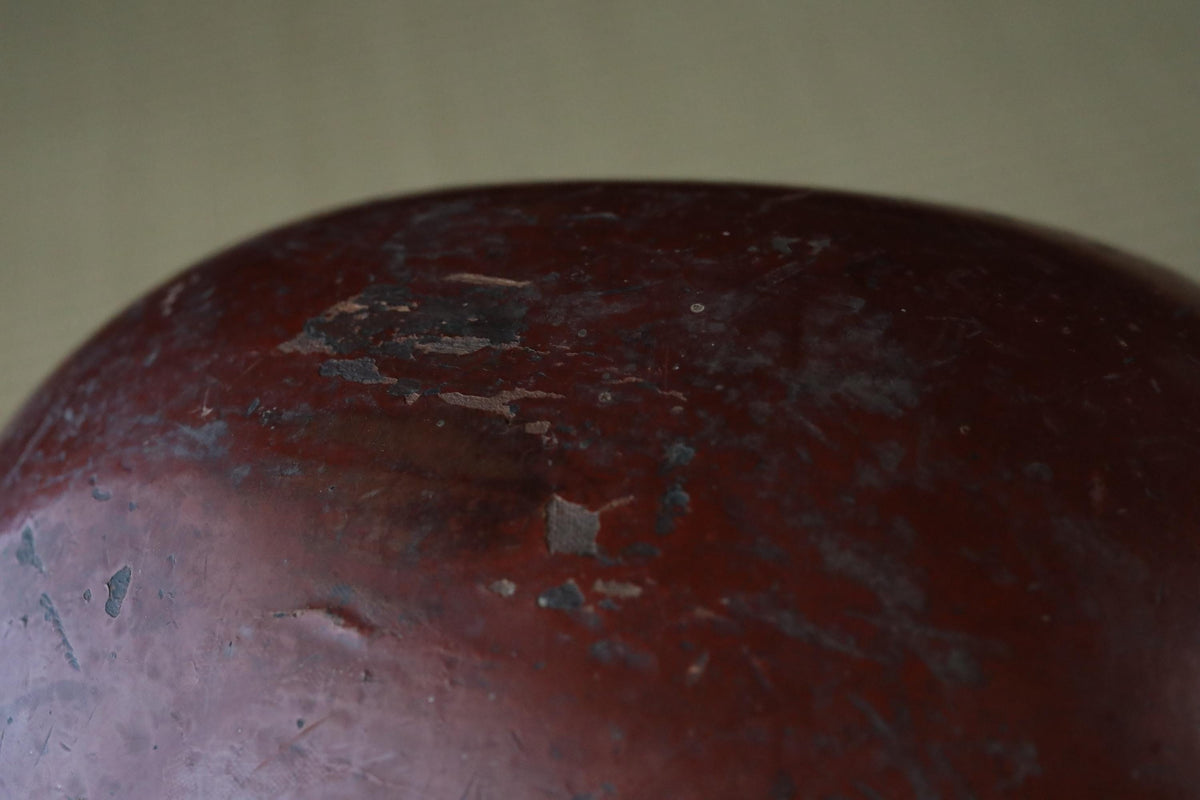 A close-up view of a red, weathered metal surface with visible scratches and rust.
