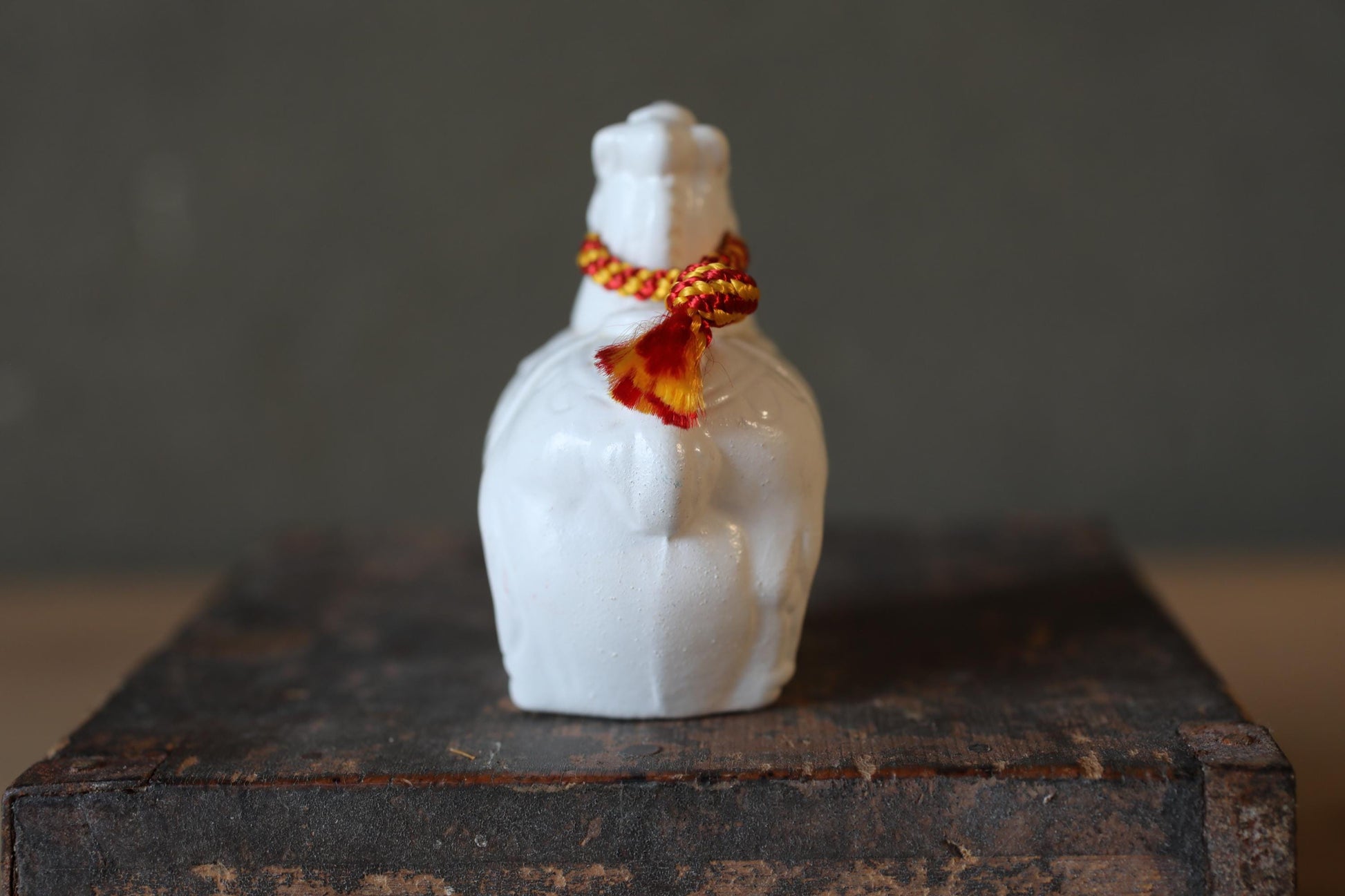 A white ceramic object with a red and yellow decorative element, placed on a wooden surface against a gray background.