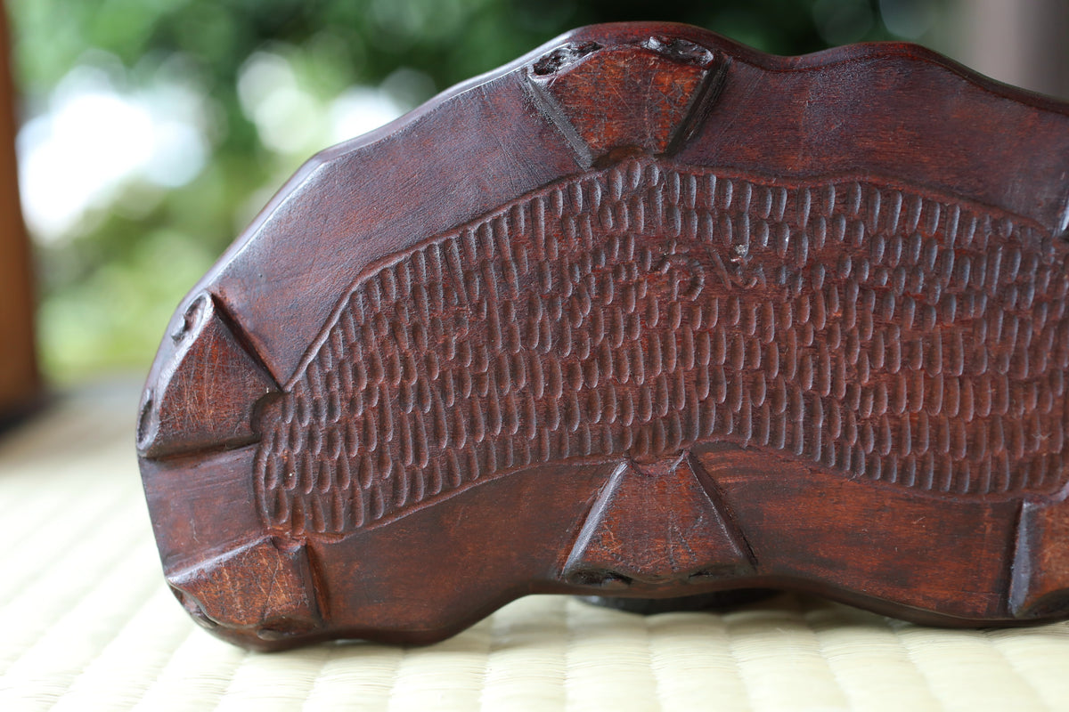 A close-up view of a wooden sculpture with a textured surface, featuring a carved pattern and a dark brown color.