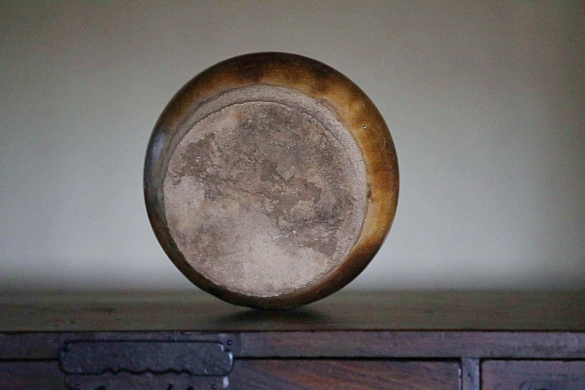 A round, brown vase with a textured surface sits on a wooden surface.