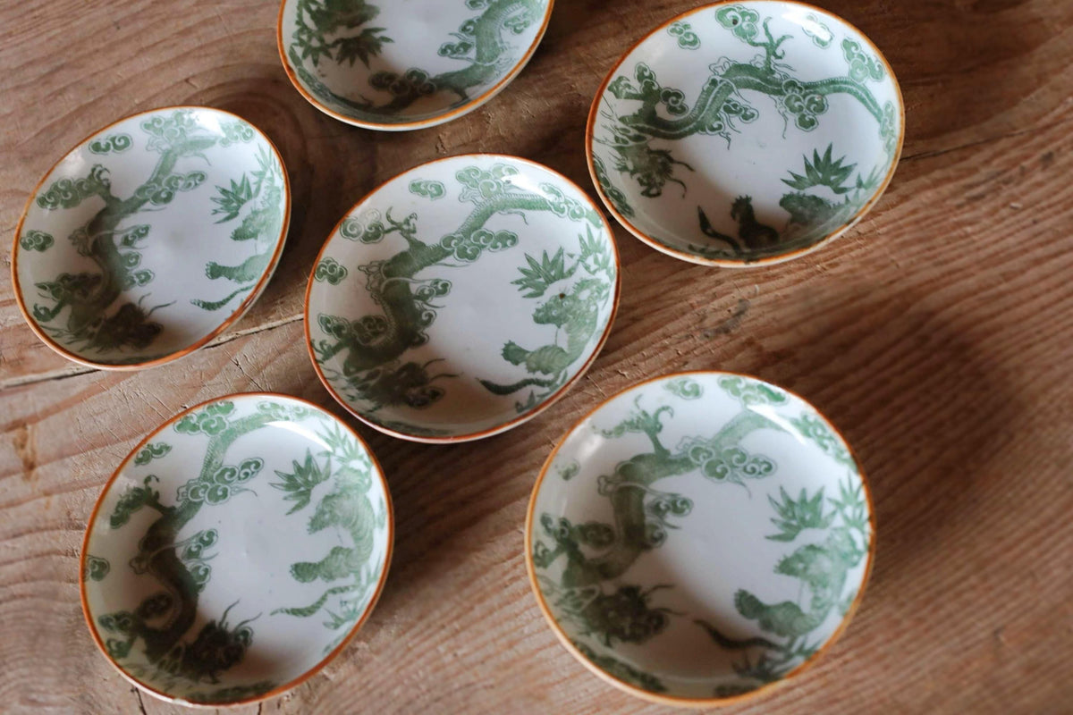 a collection of six ornate ceramic bowls with green floral designs, arranged on a wooden surface.