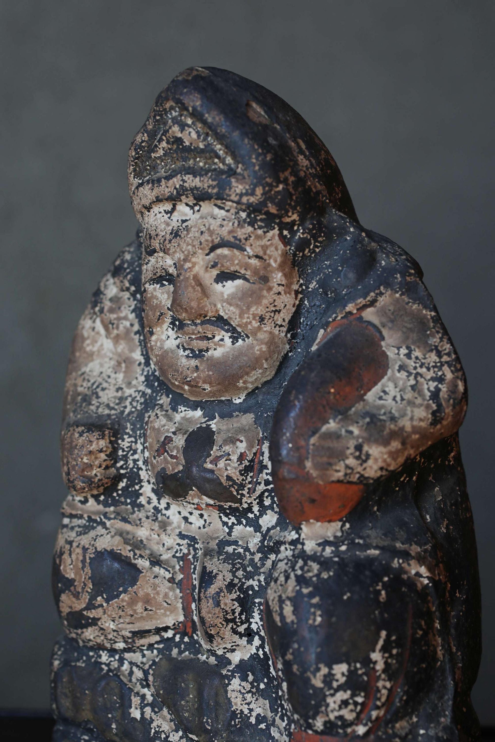 An old, weathered statue of a man with a hat and a beard, sitting and looking down.