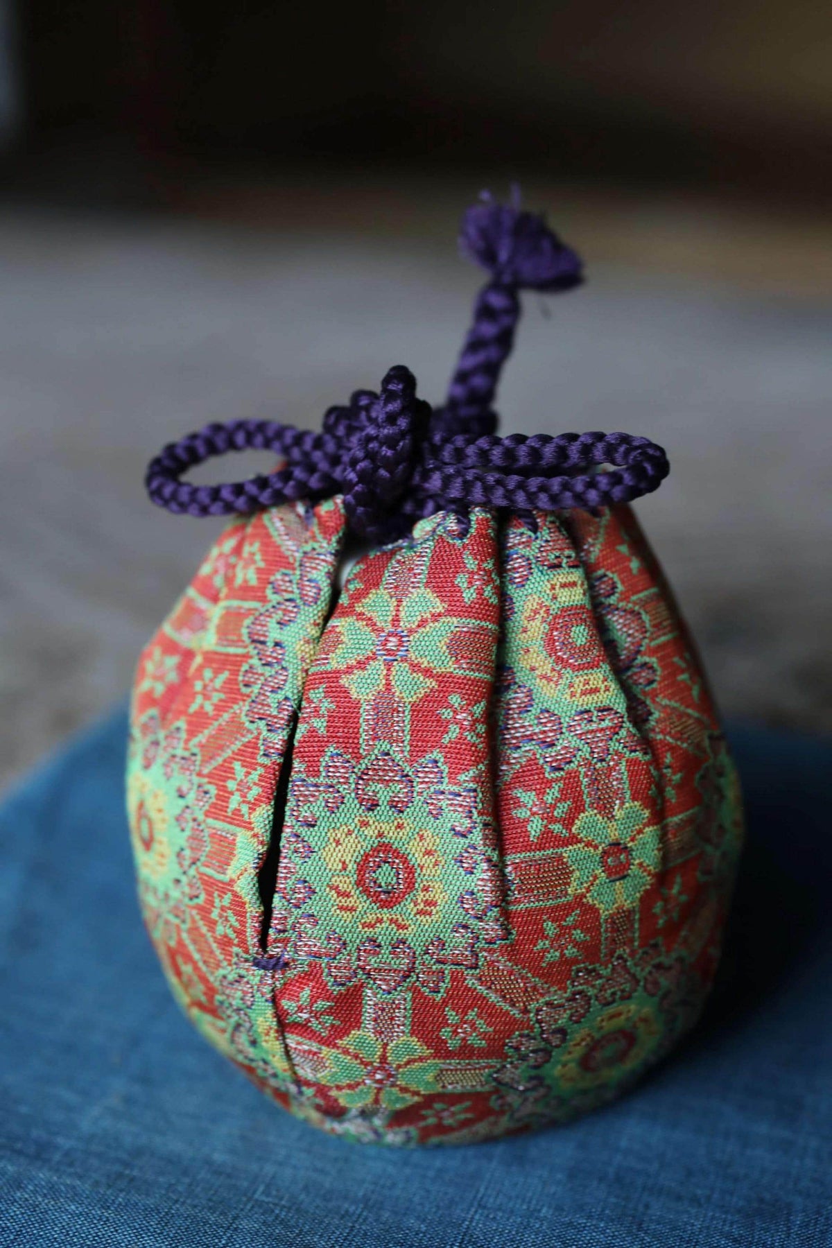 A colorful, patterned fabric bag with a purple string tied around it, sitting on a blue surface.