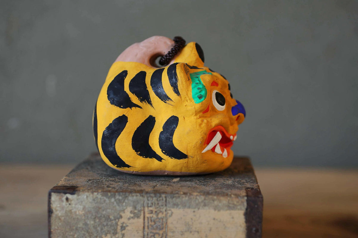 A colorful ceramic figurine of a tiger's head is displayed on a wooden surface.