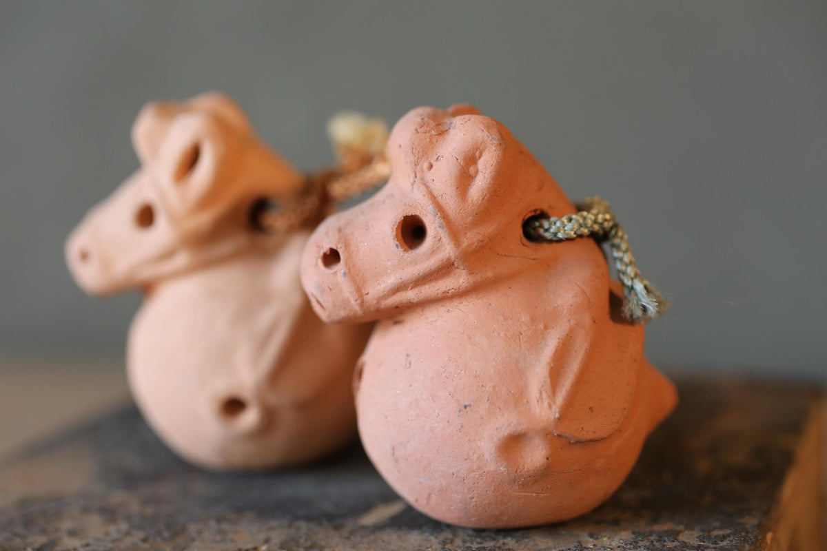 Two small, orange-colored clay figurines of animals, possibly pigs, sitting on a gray surface.
