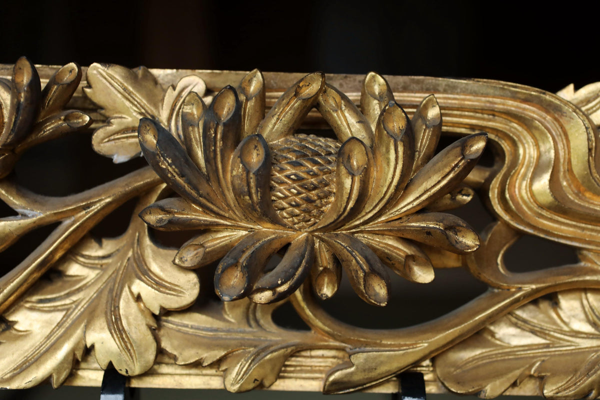 a close-up view of a decorative golden flower with intricate details, including leaves and petals, against a dark background.