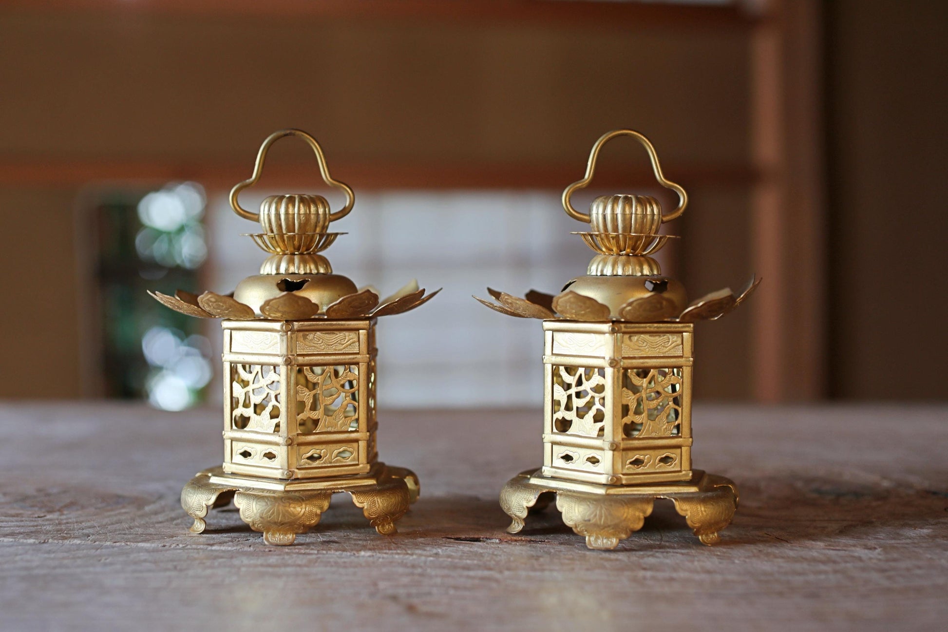 Two ornate golden lanterns with intricate designs are displayed on a wooden surface.