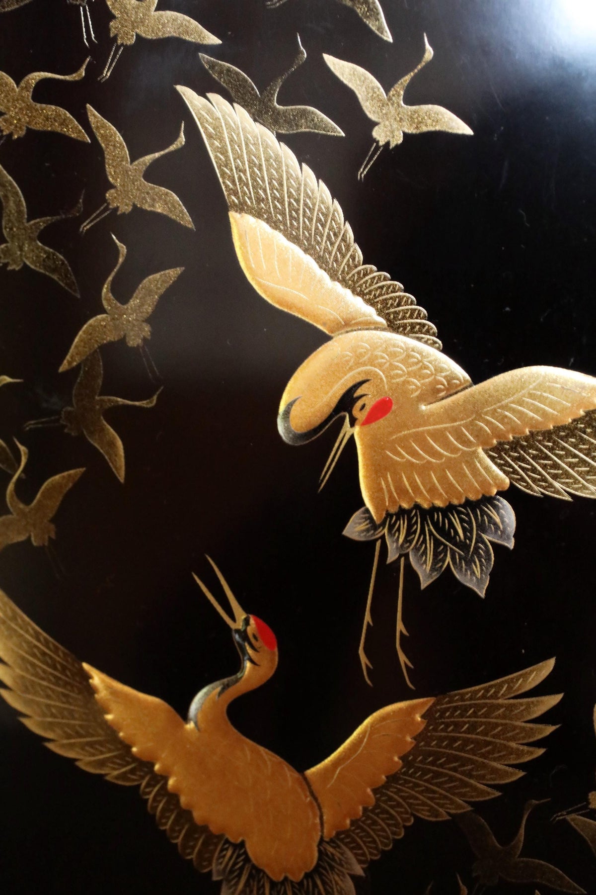 a close-up view of a pair of golden cranes with outstretched wings against a dark background.