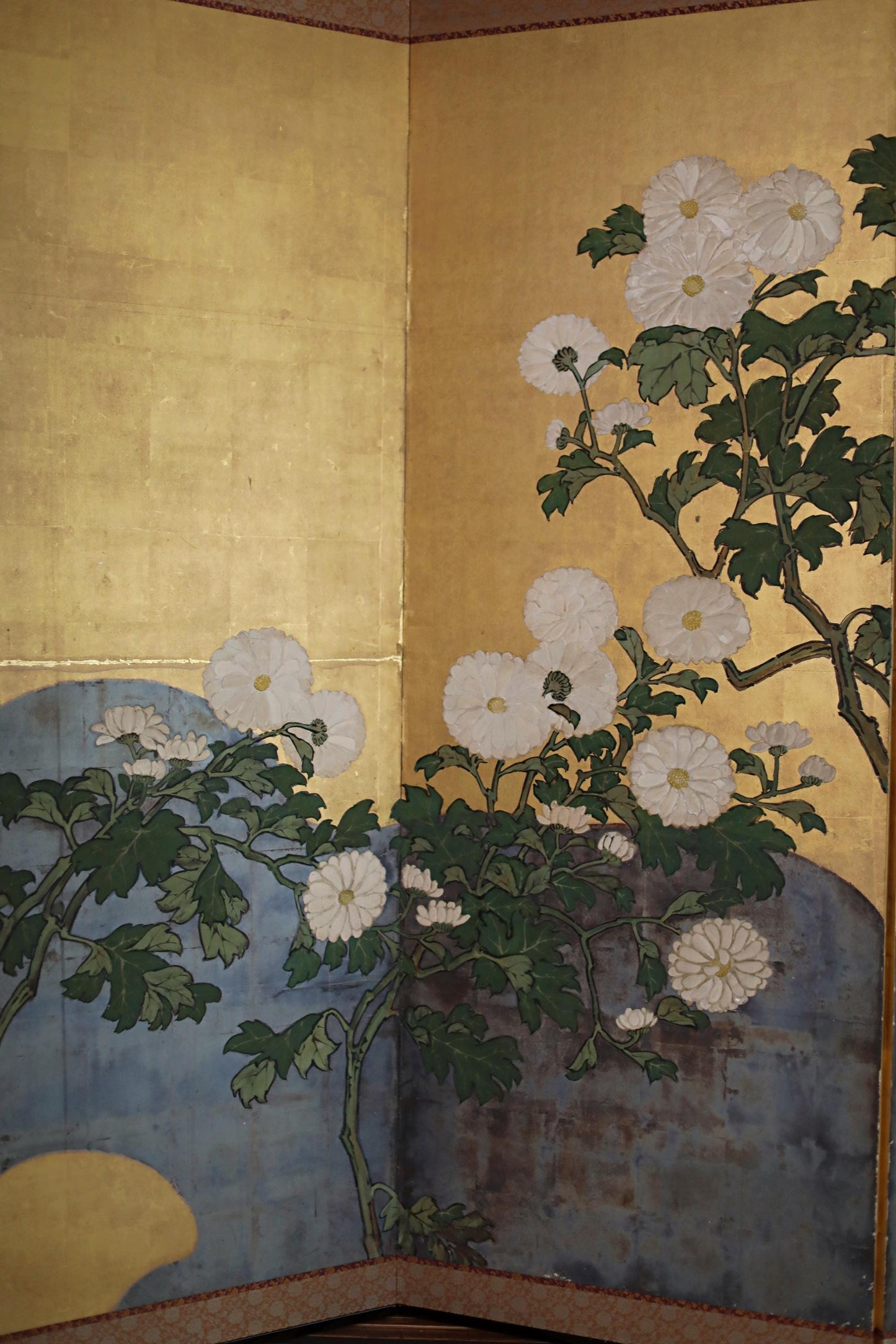 The image is a large, intricate painting featuring a variety of flowers and foliage, including white and green elements, set against a golden background.