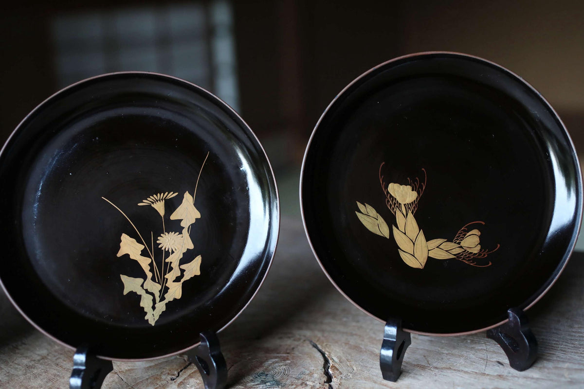 two black plates with gold designs on them, placed on a wooden surface.
