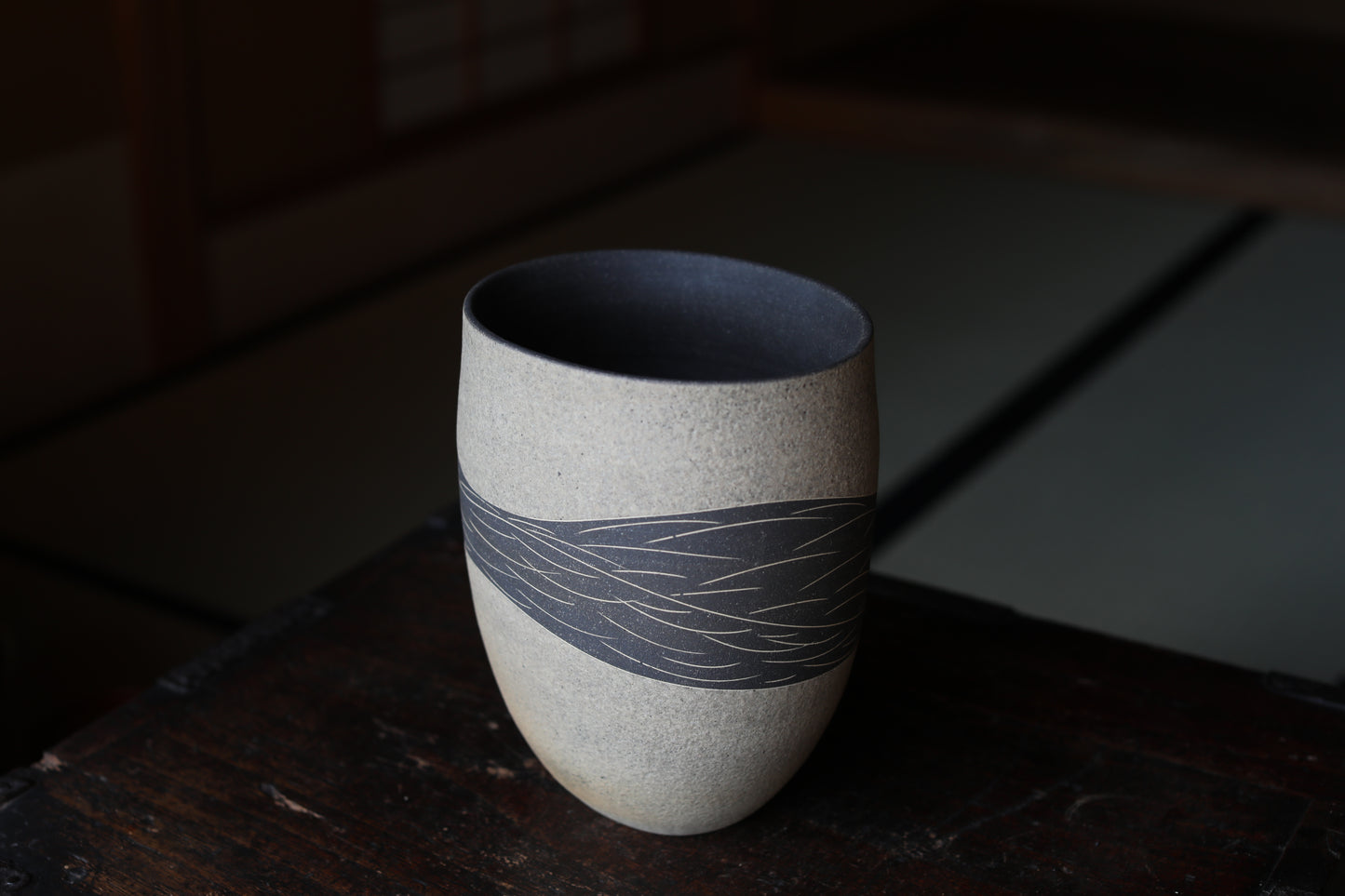 A ceramic vase with a black interior and a gray exterior, featuring a decorative pattern, sits on a wooden surface.